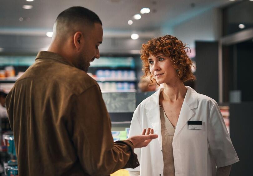 Pharmacist advises a customer, he shows her his hand