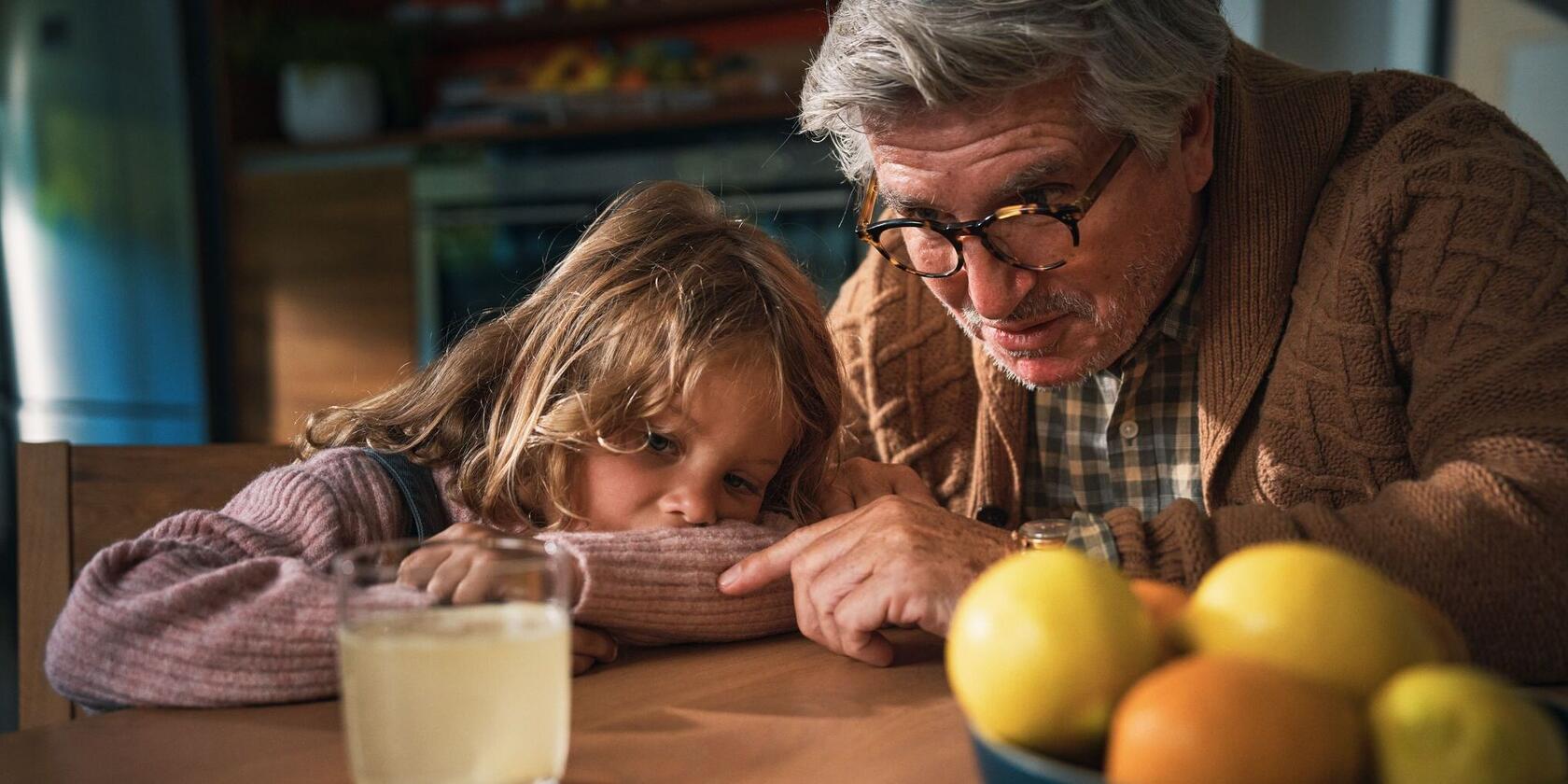 Un homme âgé et une petite fille regardent ensemble un verre d'eau contenant un comprimé effervescent.